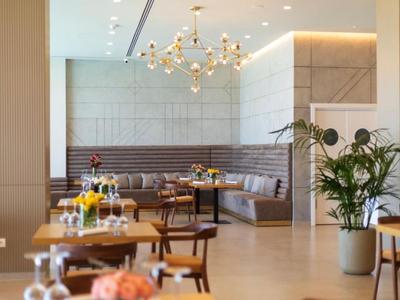 Espace de restauration d'hôtel lumineux avec tables, chaises, éclairage moderne et plantes.