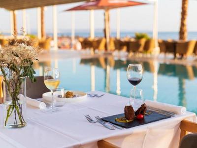 Eleganter Tisch mit weißen Tüchern, Wein, Blumen und Dessert am Pool mit Palmen und Sonnenschirmen.