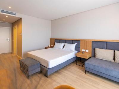 Helles, modernes Hotelzimmer mit Doppelbett, Sofa, Holzboden und schlichtem Wanddesign.