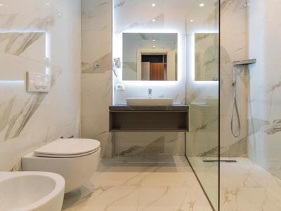 Modernes Badezimmer mit Marmorfliesen, beleuchtetem Spiegel, Toilette, Bidet und Glasduschkabine.