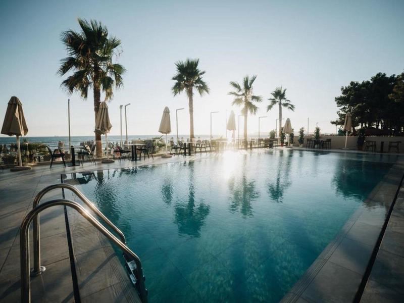 Pool mit klarem Wasser, Palmen und Sonnenschirmen am Strand bei Sonnenuntergang.