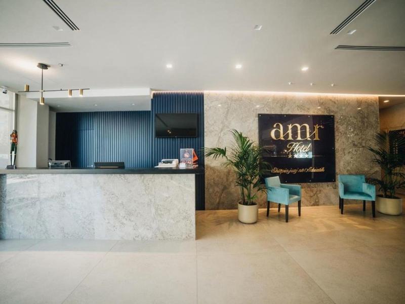 Moderner Empfangsbereich mit Marmor-Tresen, blauen Sesseln, Pflanze und beleuchtetem Logo an Wand.