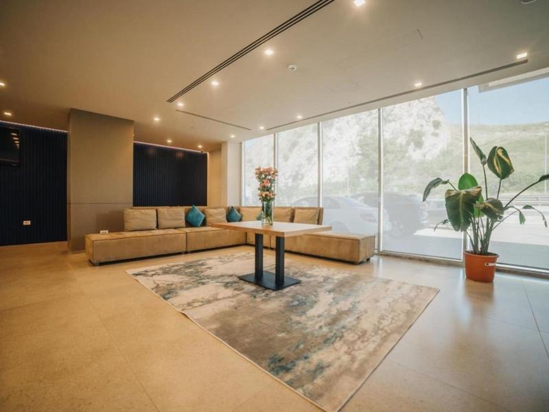 Moderner heller Wohnraum mit großer Fensterfront, beige L-förmiger Couch, Teppich und Pflanzen.