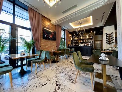 Nowoczesny bar hotelowy z elegancką marmurową podłogą, zielonymi krzesłami i dużymi oknami.