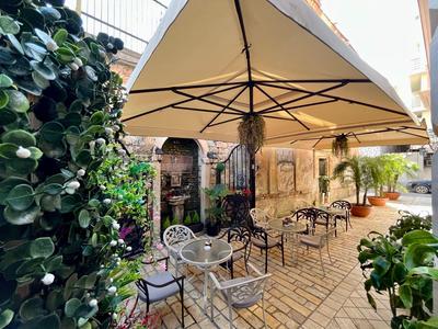 Zapraszający taras na zewnątrz z stolikami, krzesłami i parasolem obok zielonych roślin.