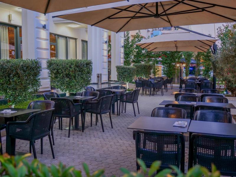 Venkovní terasa restaurace s stolky, židlemi a velkými slunečníky podél budovy.