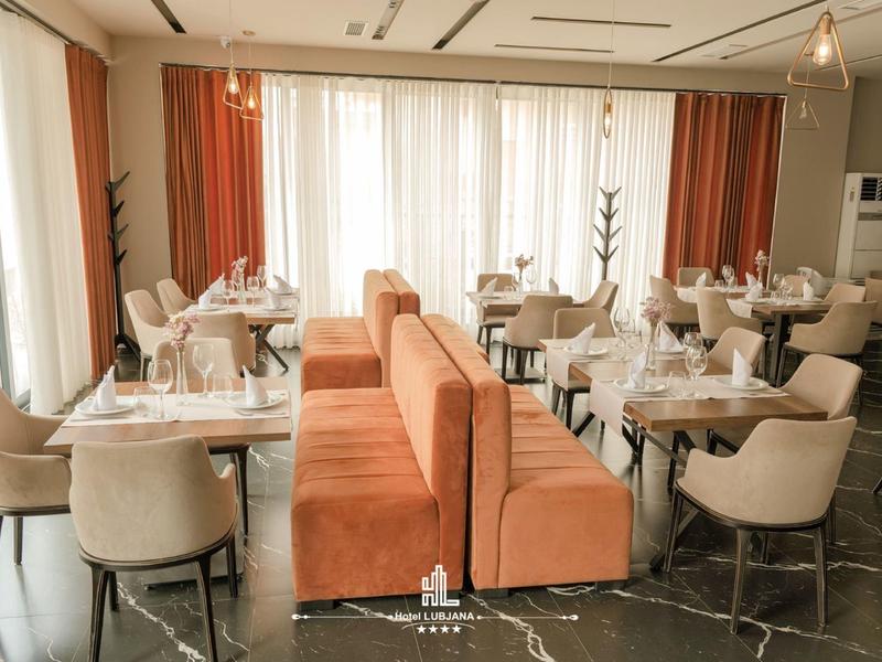 Moderně zařízená restaurace s béžovými židlemi a oranžovými lavicemi u velkých oken.