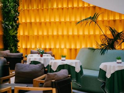 Eleganter Sitzbereich mit grünen Sesseln, weißen Tischdecken und warm beleuchtetem Akzentwanddesign.