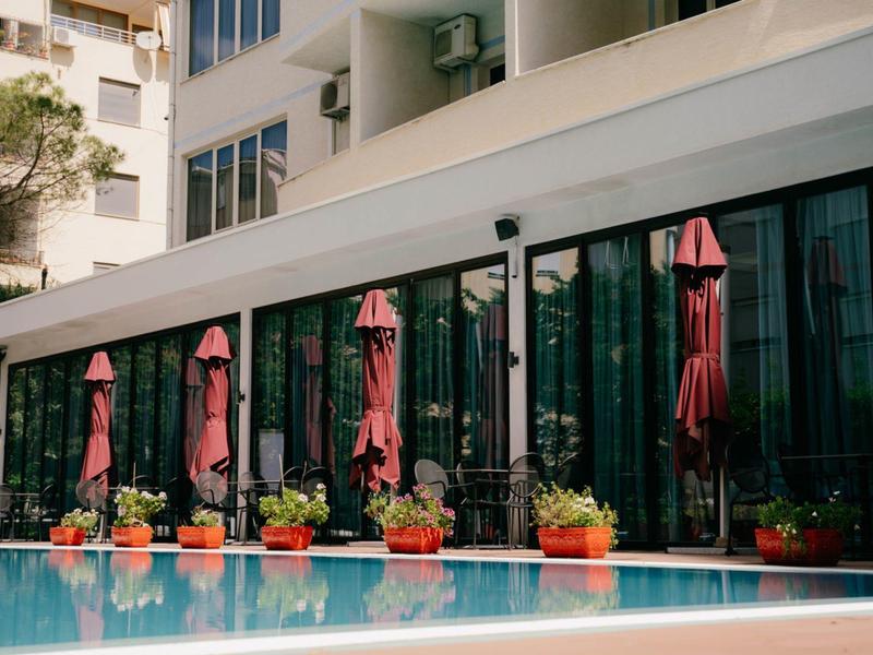 Modern hotel pool with closed red umbrellas and potted plants along the edge.