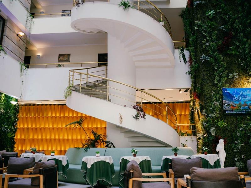 Modern hotel lobby with white spiral staircase, green plants, and stylish seating area.