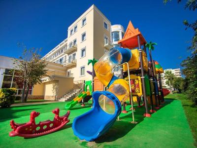 Kolorowy plac zabaw dla dzieci z zjeżdżalnią, huśtawką i wahadłem przed wielopiętrowym hotelem.
