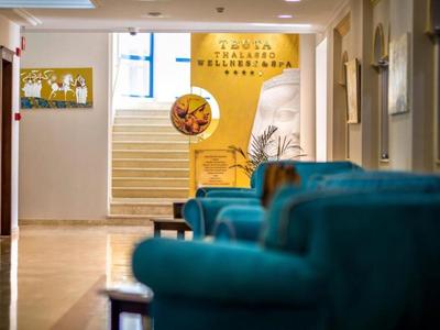 Interno di una hall d'hotel con poltrone blu, scala e cartello di benvenuto.