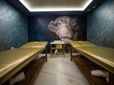 Nowoczesny pokój spa z dwoma stołami do masażu i ciemnymi ścianami z artystycznym malowidłem.