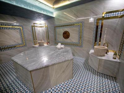 Tradycyjna łaźnia hamam z centralnym marmurowym bloczkiem i wyłożonymi kafelkami ścianami i podłogą.