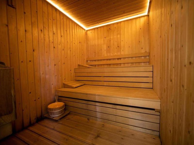 Wnętrze sauny z drewnianymi ścianami i wielopoziomowymi drewnianymi ławkami pod ciepłym oświetleniem.