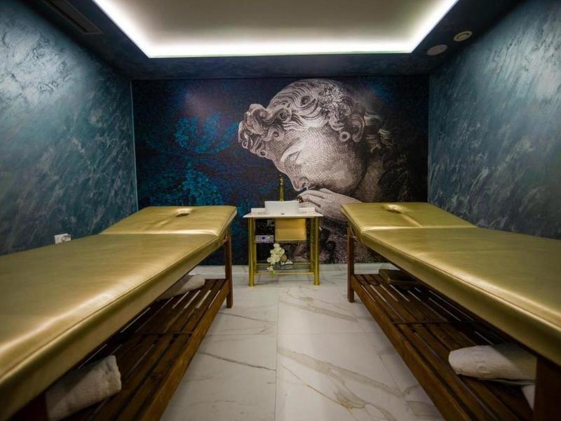 Nowoczesny pokój spa z dwoma stołami do masażu i ciemnymi ścianami z artystycznym malowidłem.