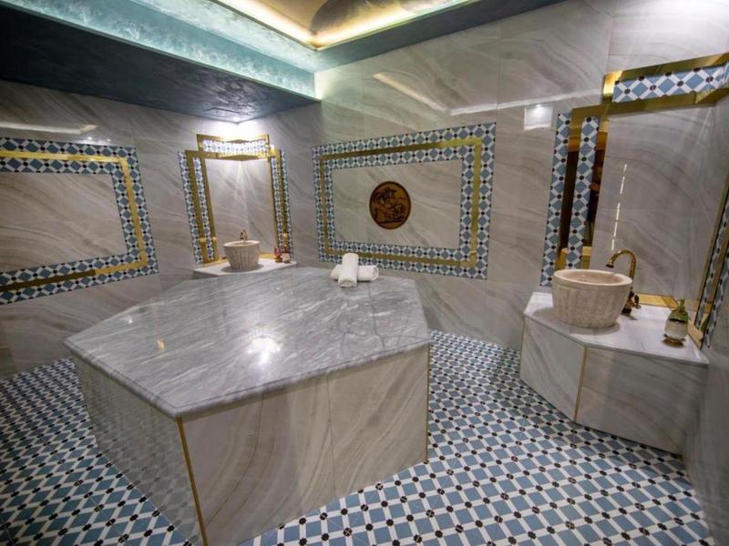 Tradycyjna łaźnia hamam z centralnym marmurowym bloczkiem i wyłożonymi kafelkami ścianami i podłogą.
