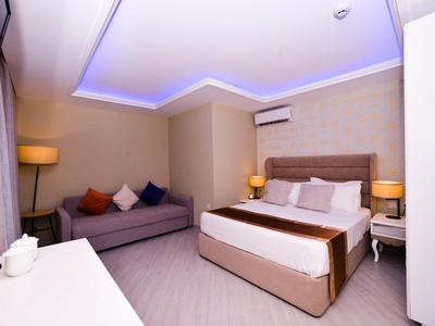 Modernes Hotelzimmer mit Doppelbett, Sofa, Nachttischen und indirekter Beleuchtung an der Decke.