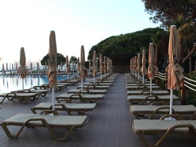 Sillones vacíos y sombrillas cerradas a lo largo de un muelle de madera junto a la piscina.