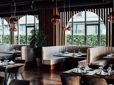 Restaurante moderno con áreas de asientos elegantes y grandes ventanas con vista al área verde.