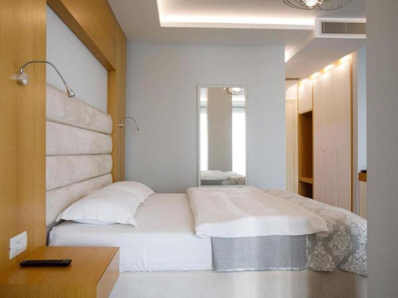 Camera d'hotel moderna con letto matrimoniale, grande specchio e illuminazione calda.