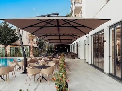 Area esterna moderna di un hotel con posti a sedere e piscina sotto grandi ombrelloni.