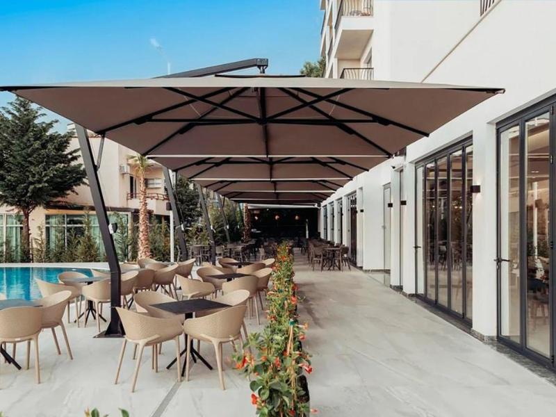 Area esterna moderna di un hotel con posti a sedere e piscina sotto grandi ombrelloni.