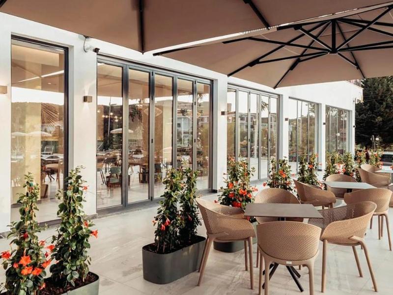 Terrazza di un ristorante moderno con tavoli rotondi, sedie e grandi ombrelloni.
