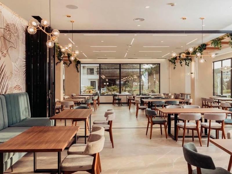 Ristorante moderno con tavoli in legno, sedie imbottite verdi e grandi finestre per la luce naturale.