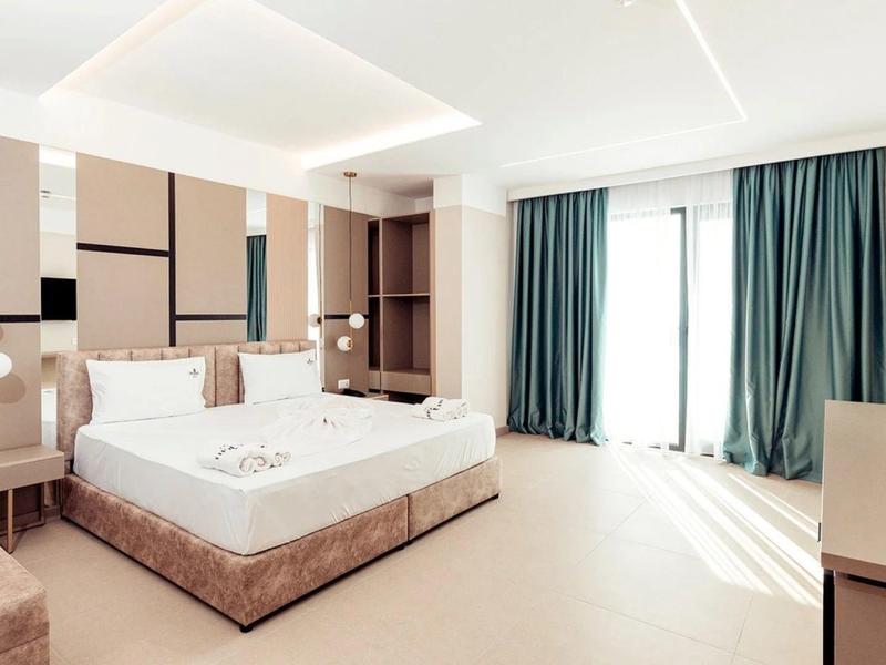 Camera d'hotel luminosa con letto matrimoniale, poltrone, scrivania e grandi finestre con tende.