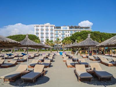 Strand met ligbedden, rieten parasols en een hotelgebouw op de achtergrond bij heldere lucht.