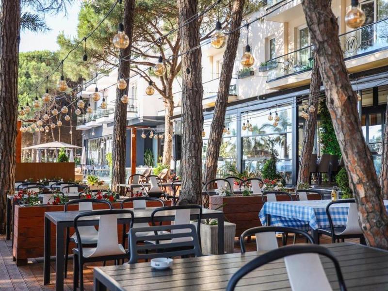 Ristorante all'aperto con tavoli, sedie e alberi davanti a un edificio.