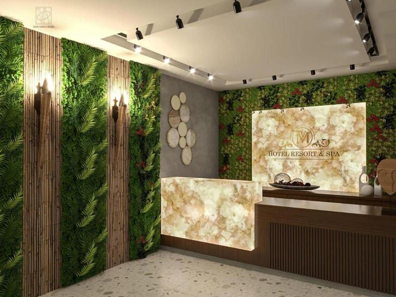 Area reception moderna dell'hotel con bancone illuminato e pareti verdi verticali.