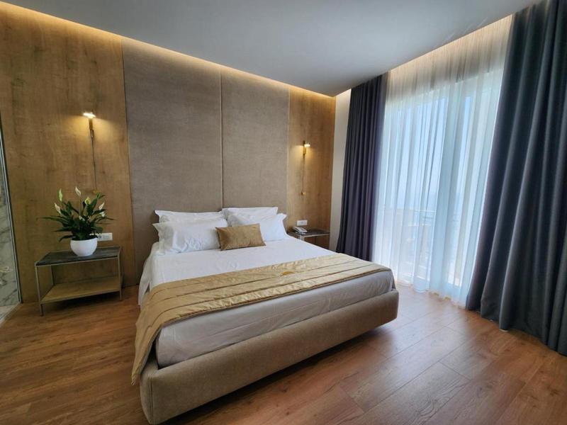 Nowoczesna sypialnia z dużym łóżkiem, drewnianą podłogą i zasłonami na wysokich oknach.