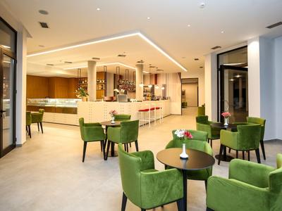 Modern hotel bar area with green chairs and round tables in a bright, spacious room.