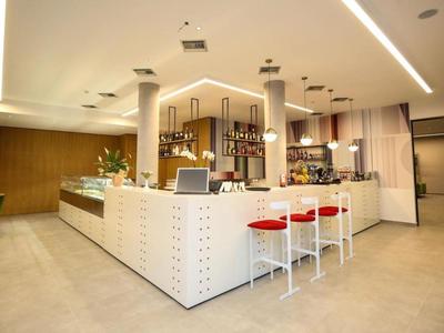 Modern hotel bar area with white counter, red bar stools, and elegant lighting.