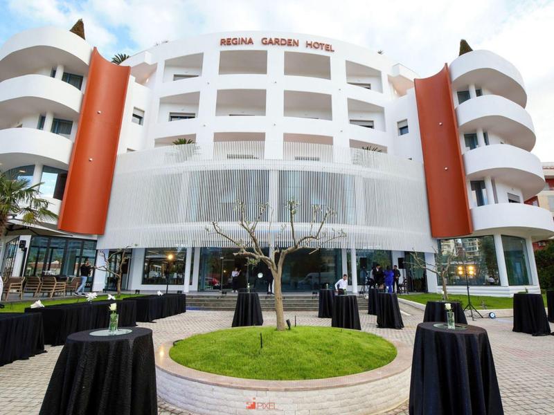 Exterior view of a white hotel with round balconies and standing tables in front.
