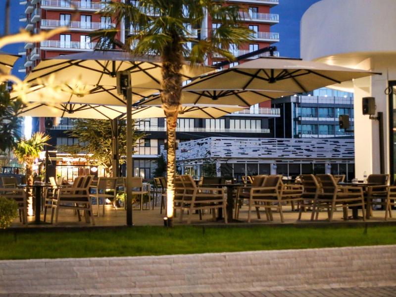 Illuminated outdoor hotel terrace with tables, chairs, and umbrellas at dusk.