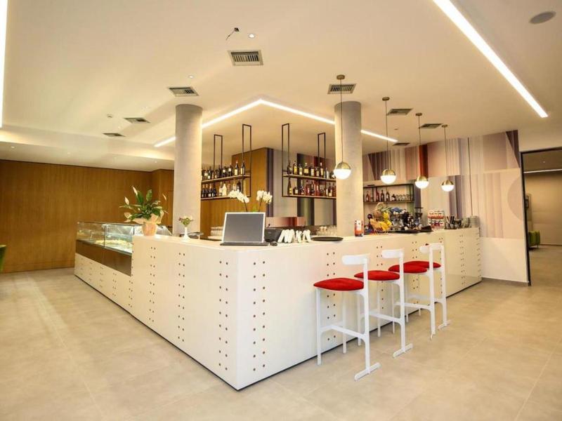 Modern hotel bar area with white counter, red stools, and minimalist lighting.