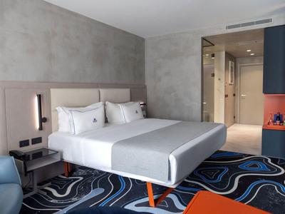 Camera d'albergo moderna con letto matrimoniale, pareti grigie e moquette colorata.