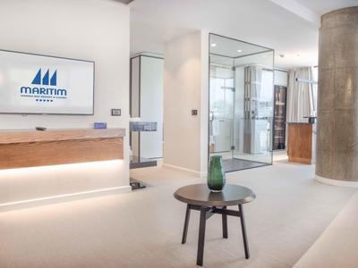 Moderna hall d'hotel con posti a sedere, TV e ampia finestra che lascia entrare la luce naturale.