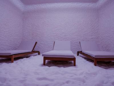 Tre lettini in legno con cuscini in una stanza con pareti e pavimento bianchi simili a sale.