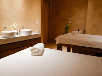 Sala trattamenti con due lettini da massaggio e asciugamani arrotolati in spa illuminata caldamente.