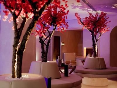 Sala de hotel moderna con áreas de asientos redondos y arreglos florales rojos decorativos.