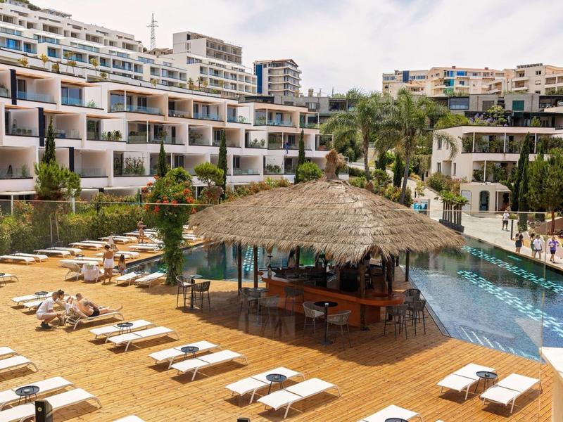 Piscina moderna dell'hotel con lettini, ombrelloni e bar esterno coperto.