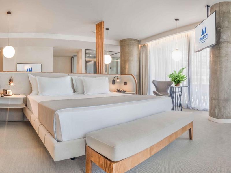 Camera d'hotel moderna con letto grande, tende chiare e TV a muro.