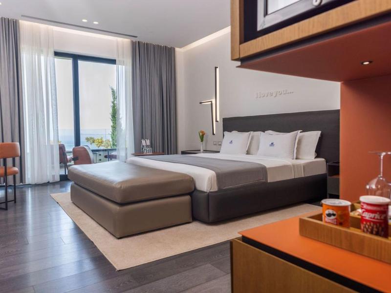 Camera d'hotel moderna con grande letto matrimoniale, zona salotto e vista sul balcone.