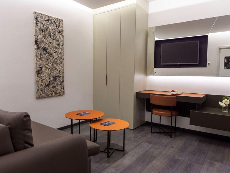 Camera moderna con divano, due piccoli tavoli e zona lavoro con sedia e specchio.