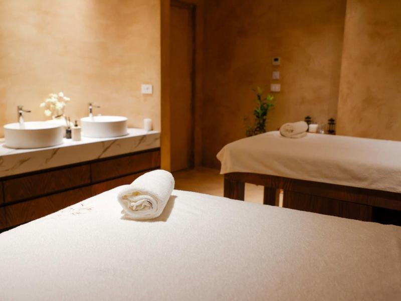 Sala trattamenti con due lettini da massaggio e asciugamani arrotolati in spa illuminata caldamente.