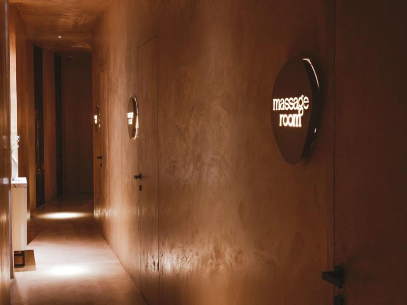 Corridoio d'hotel scuro con un'insegna luminosa 'Massage Room' sulla parete.